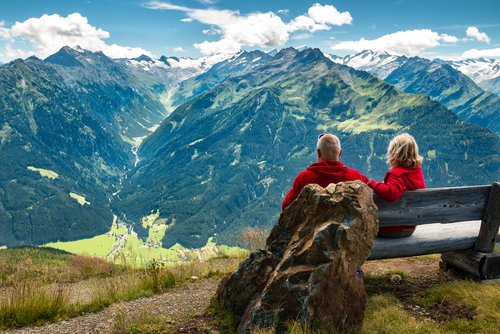 older couple sitting on bench looking at mountains 
