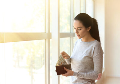 woman standing in front of window while taking money out of her wallet 