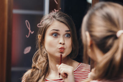 woman holding pencil while looking into a mirror