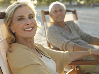 husband and wife sitting on chairs at beach while holding hands